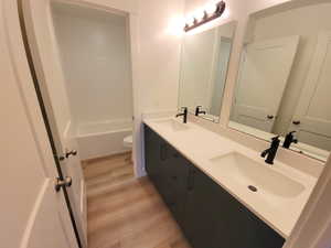 Full bathroom featuring double vanity, light wood-style flooring, and tub / shower combination