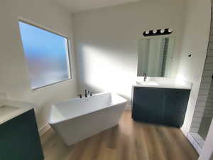 Full bathroom with two vanities, a soaking tub, and dark wood-style flooring