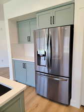 Kitchen with stainless steel fridge with ice dispenser, light wood-style floors, and green cabinetry
