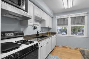 Kitchen with gas range, white cabinetry, original hardwood flooring, stainless steel microwave, and white dishwasher