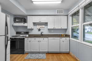 Kitchen featuring white cabinets, granite countertops, black gas stove, dishwasher, and original hardwood flooring