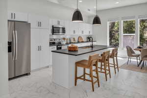 Kitchen with appliances with stainless steel finishes, decorative backsplash, light marble finish floors, a center island with sink, and recessed lighting