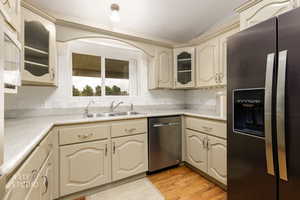 Kitchen with stainless steel appliances, glass insert cabinets, cream cabinets, and light wood-type flooring