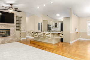 Kitchen featuring open floor plan, light wood-style flooring, cream cabinetry, lofted ceiling, and a brick fireplace
