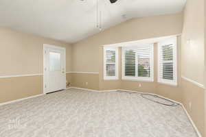 Carpeted empty room featuring a ceiling fan and vaulted ceiling