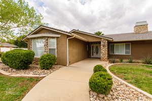 Ranch-style house with stucco siding, a chimney, a front lawn, and stone siding