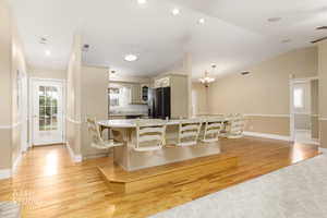 Kitchen with cream cabinets, light wood-style flooring, black refrigerator with ice dispenser, recessed lighting, and lofted ceiling