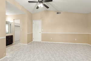 Unfurnished bedroom featuring light carpet, vaulted ceiling, light tile patterned floors, connected bathroom, and a ceiling fan