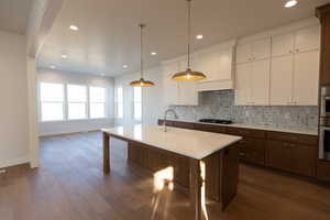 Two tone kitchen with dual tone cabinetry, decorative backsplash, hanging light fixtures, dark wood finished floors, and an island with sink