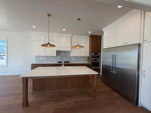 Kitchen featuring stainless steel appliances, white cabinets, hanging light fixtures, a kitchen island with sink, and a textured ceiling