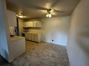 Kitchen featuring light countertops, white appliances, white cabinets, ceiling fan, and under cabinet range hood