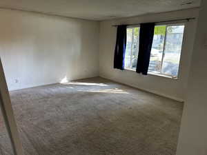 Spacious living area featuring large front windows, natural light, and neutral carpet flooring.