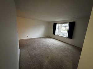 Bright and spacious living area featuring large front window, fresh interior paint, and neutral carpet flooring.