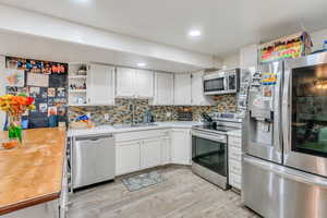 Kitchen featuring stainless steel appliances, decorative backsplash, white cabinetry, open shelves, and light wood-style flooring