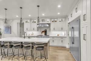 Kitchen featuring white cabinetry, built in refrigerator, glass insert cabinets, recessed lighting, and decorative light fixtures