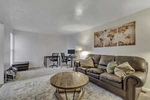 Carpeted living area featuring a desk and a textured ceiling