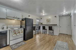 Kitchen featuring black appliances, a textured ceiling, light wood-type flooring, under cabinet range hood, and a kitchen breakfast bar