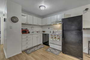 Kitchen with black appliances, a textured ceiling, light countertops, white cabinets, and light wood finished floors