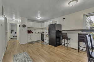 Kitchen featuring black appliances, a textured ceiling, light wood-type flooring, white cabinets, and light countertops