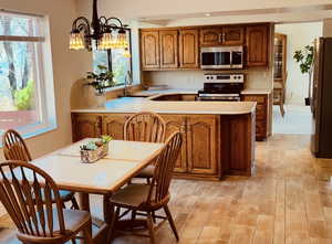 Kitchen featuring light countertops, stainless steel appliances, hanging lights, wood finish cabinets, and light wood finished floors