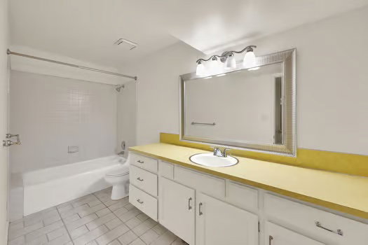 Basement Apartment Bathroom with extra wide vanity, shower / bath combination, large mirror and light tile patterned flooring.