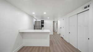 Kitchen featuring light wood-style floors, freestanding refrigerator, a peninsula, light stone countertops, and recessed lighting