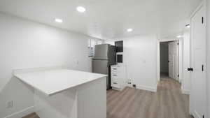 Kitchen featuring light countertops, a peninsula, freestanding refrigerator, light wood-style flooring, and recessed lighting