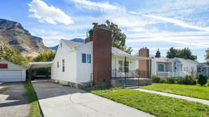 Bungalow-style house featuring an outbuilding, a front lawn, a porch, concrete driveway, and a chimney