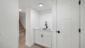 Bar area with white cabinets, light wood-style floors, stairs, and light stone countertops