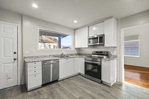 Kitchen featuring stainless steel appliances, white cabinets, light stone countertops, light wood finished floors, and recessed lighting