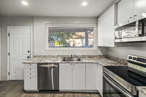 Kitchen featuring stainless steel appliances, white cabinetry, recessed lighting, dark wood-style flooring, and light stone countertops