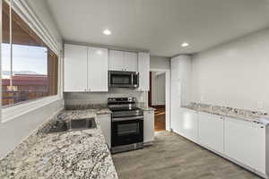Kitchen with appliances with stainless steel finishes, white cabinetry, light wood-style floors, recessed lighting, and light stone counters