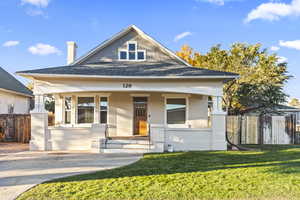 View of front facade featuring a porch, brick siding, a shingled roof, and a chimney