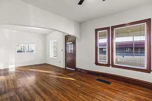 Unfurnished room with dark wood-type flooring, healthy amount of natural light, ceiling fan, and arched walkways