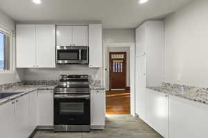 Kitchen with stainless steel appliances, white cabinets, light stone counters, and recessed lighting