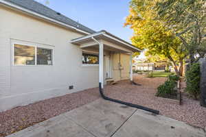 Doorway to property with crawl space, brick siding, a patio, and a shingled roof