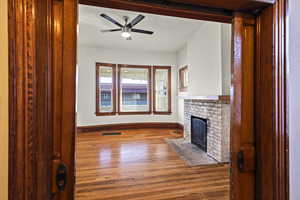 Unfurnished living room featuring wood finished floors, a brick fireplace, and a ceiling fan