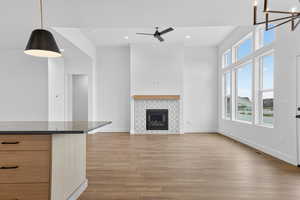 Unfurnished living room with light wood-style flooring, a tiled fireplace, recessed lighting, a ceiling fan, and a high ceiling