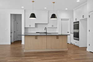 Kitchen featuring an island with sink, decorative backsplash, white cabinetry, dark wood-type flooring, and recessed lighting