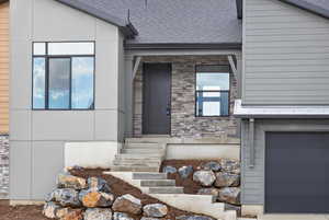 View of exterior entry featuring stone siding and a shingled roof