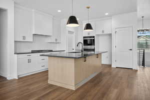 Kitchen featuring tasteful backsplash, a center island with sink, white cabinets, dark wood-type flooring, and recessed lighting