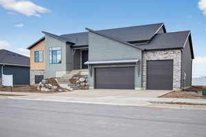 View of front of house featuring stone siding, roof with shingles, driveway, and a garage