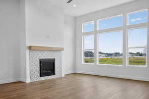 Unfurnished living room featuring a tile fireplace, wood finished floors, recessed lighting, ceiling fan, and a towering ceiling