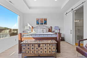 Bedroom featuring a raised ceiling, light wood finished floors, a barn door, and recessed lighting