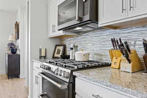Kitchen featuring appliances with stainless steel finishes, tasteful backsplash, white cabinetry, light stone countertops, and light wood-type flooring
