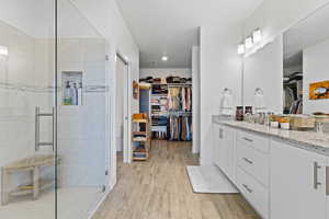 Full bath with a walk in closet, double vanity, light wood-style floors, and a shower stall