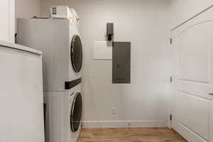 Laundry room featuring electric panel, light wood-style floors, and stacked washer / dryer