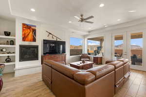 Living area featuring a fireplace, light wood-style flooring, french doors, and a ceiling fan