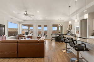Living area with light wood-style flooring, healthy amount of natural light, ceiling fan, and suspended lighting