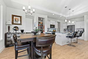 Dining room with light wood-type flooring, a tray ceiling, recessed lighting, and a chandelier